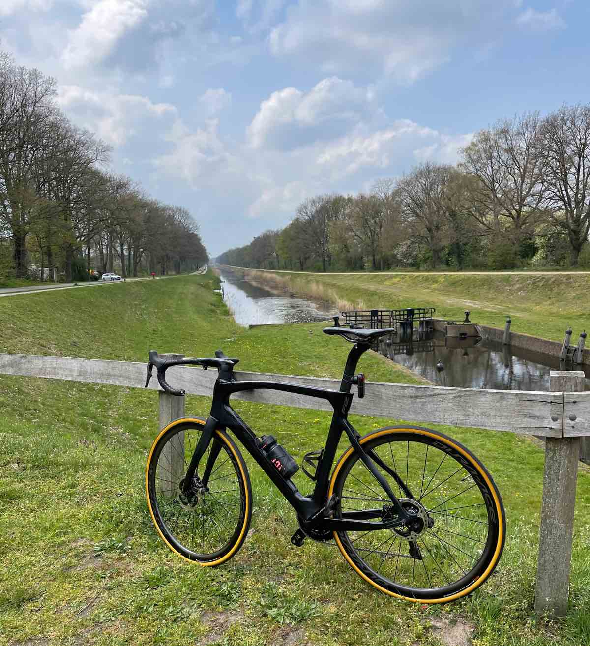 bikerumor pic of the day a road bicycle leans against a wooden fence near a cycle path that follows a canal there are trees bordering the sites of the canal.