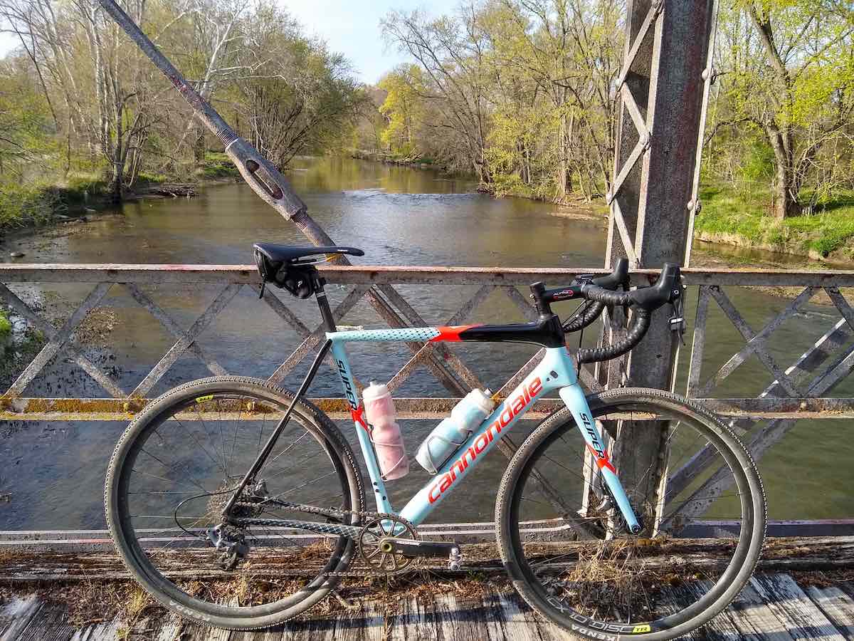 bikerumor pic of the day a carbondale gravel bike sits across a metal bridge over the eel river in indiana the trees and grass along the river banks are just beginning to green out for spring, the day is bright and sunny.