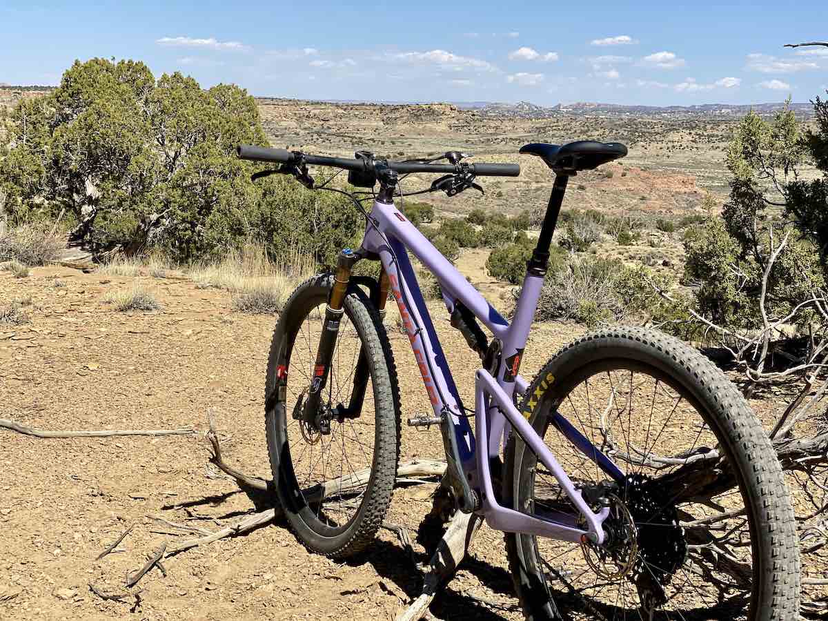 bikerumor pic of the day lavender blur mountain bike perched atop a mountain overlooking gallup new mexico. the sun is high and strong over the dirt and cedar trees along the trail.