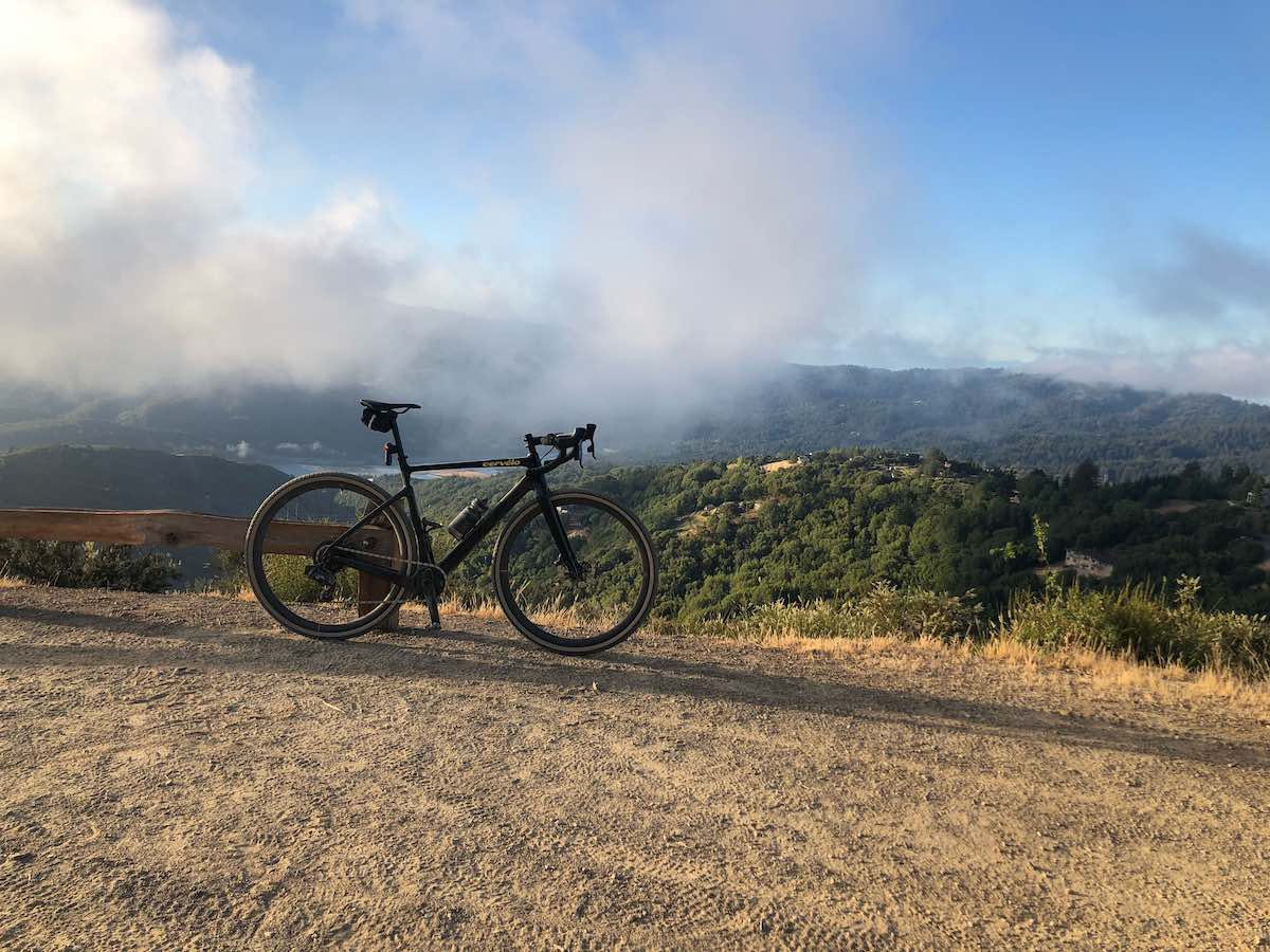 bikerumor pic of the day a bicycle is atop a clearing with clouds and mountaintops in the distance.