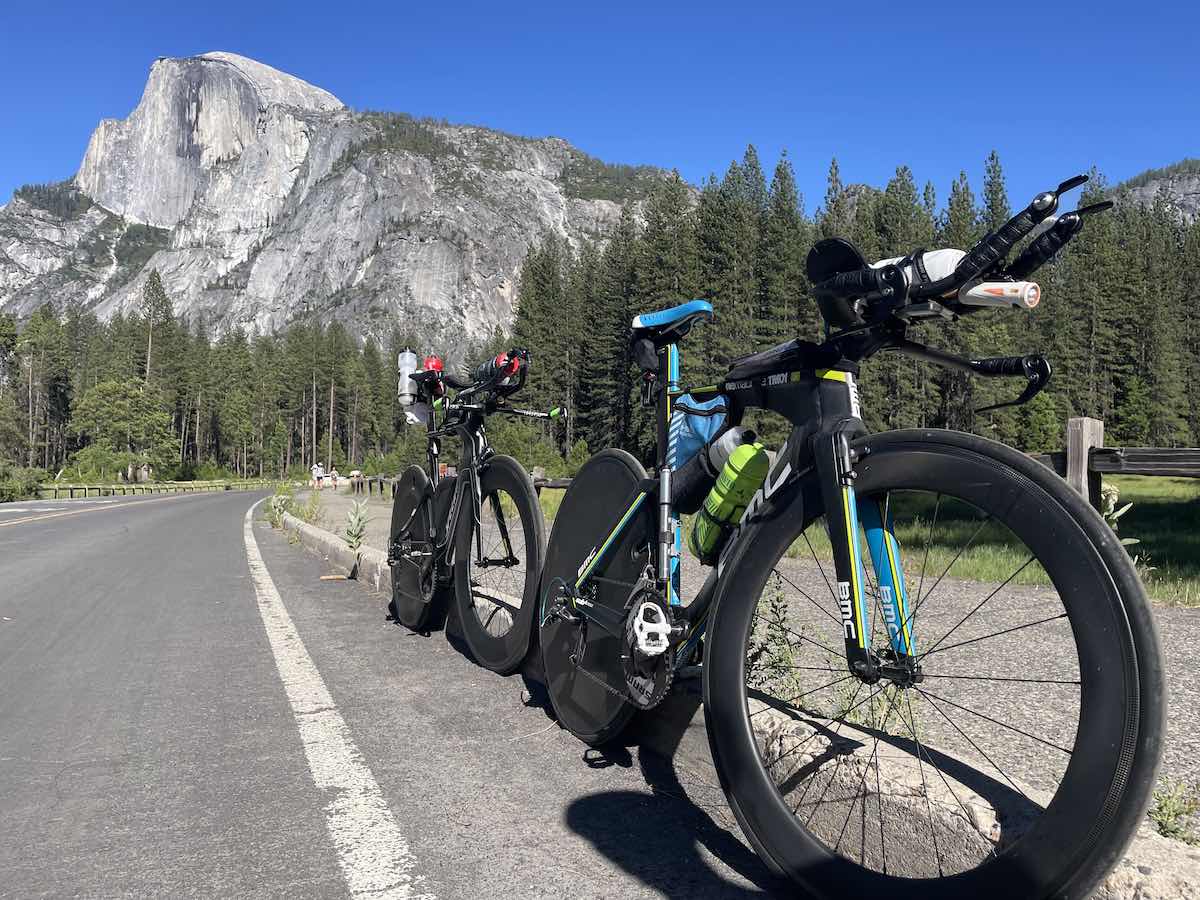 bikerumor pic of the day two road bicycles packed with bags are alongside a road with the mountains of yosemite national park california in the background. there are lots of tall pine trees and the sky is clear and blue.