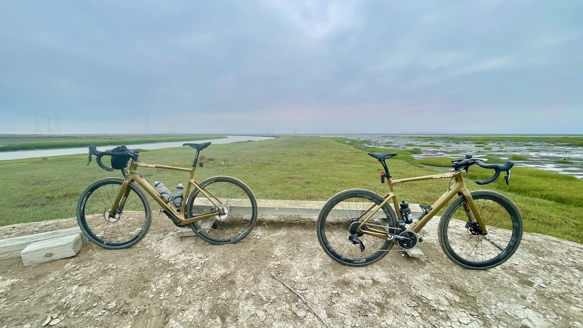 bikerumor pic of the day two gold cervelo bicycles posed in the baylands near alvero california, the land is flat with short grass and there is wetland surrounding, the sky is overcast with a slight hint of sunset in the distance.