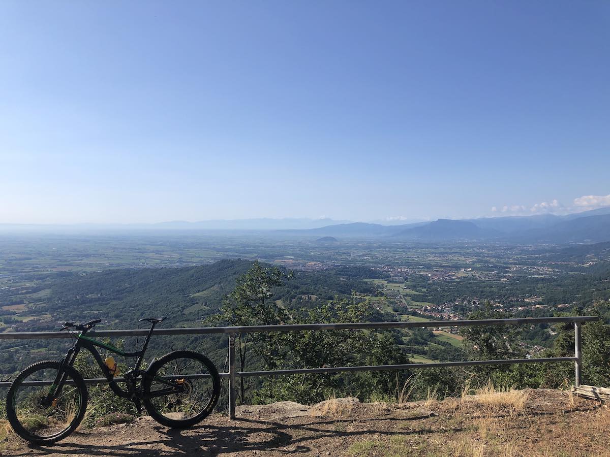 bikerumor pic of the day a bicycle leans against a metal railing overlooking a vast mountain region. the sky is clear with a slight haze over the horizon.