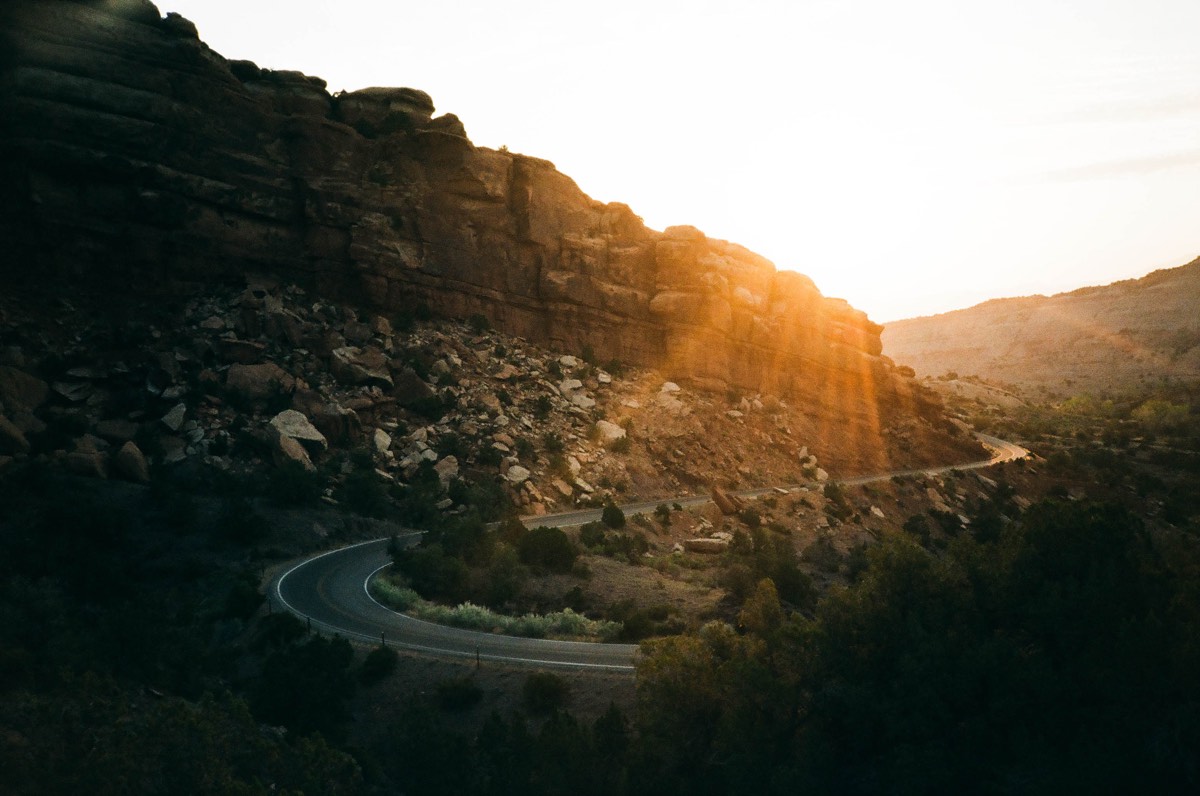bikerumor pic of the day a two lane road serpentines between high rocky cliffs as the sun rises over them.