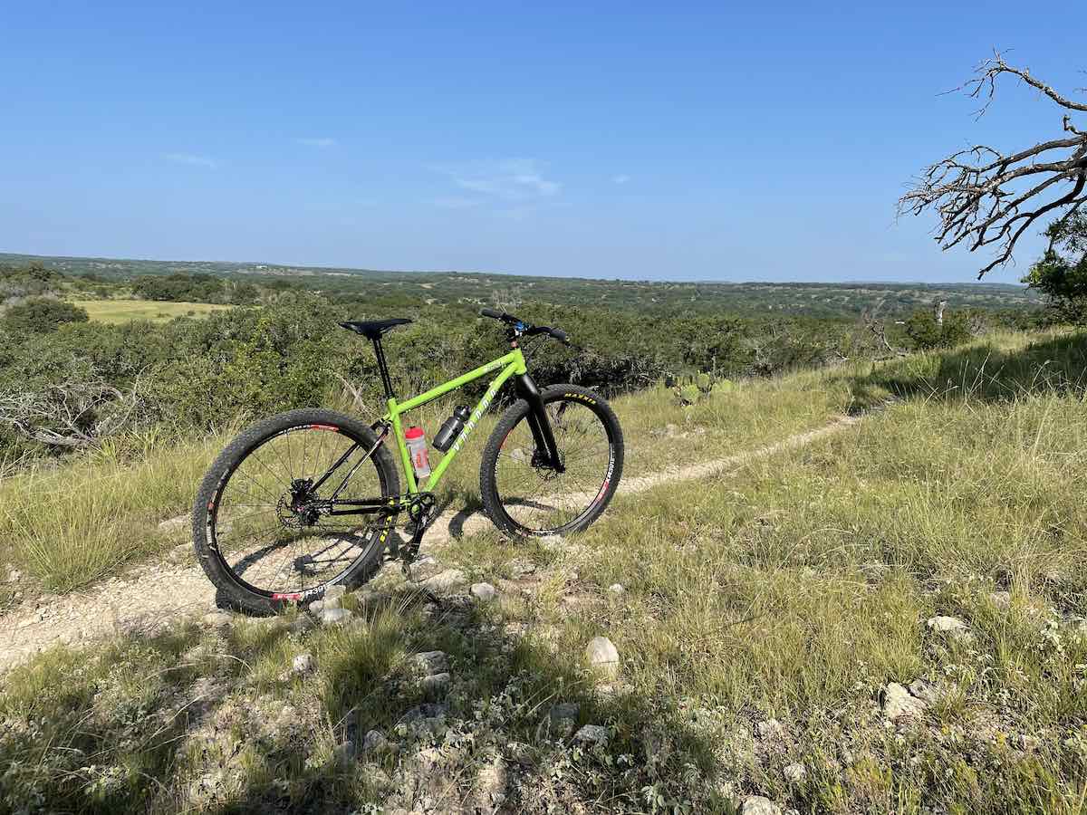 bikerumor pic of the day a mountain bike is on a narrow dirt trail on a ridge overlooking a vast flat expanse of land the sky is clear and the sun is high