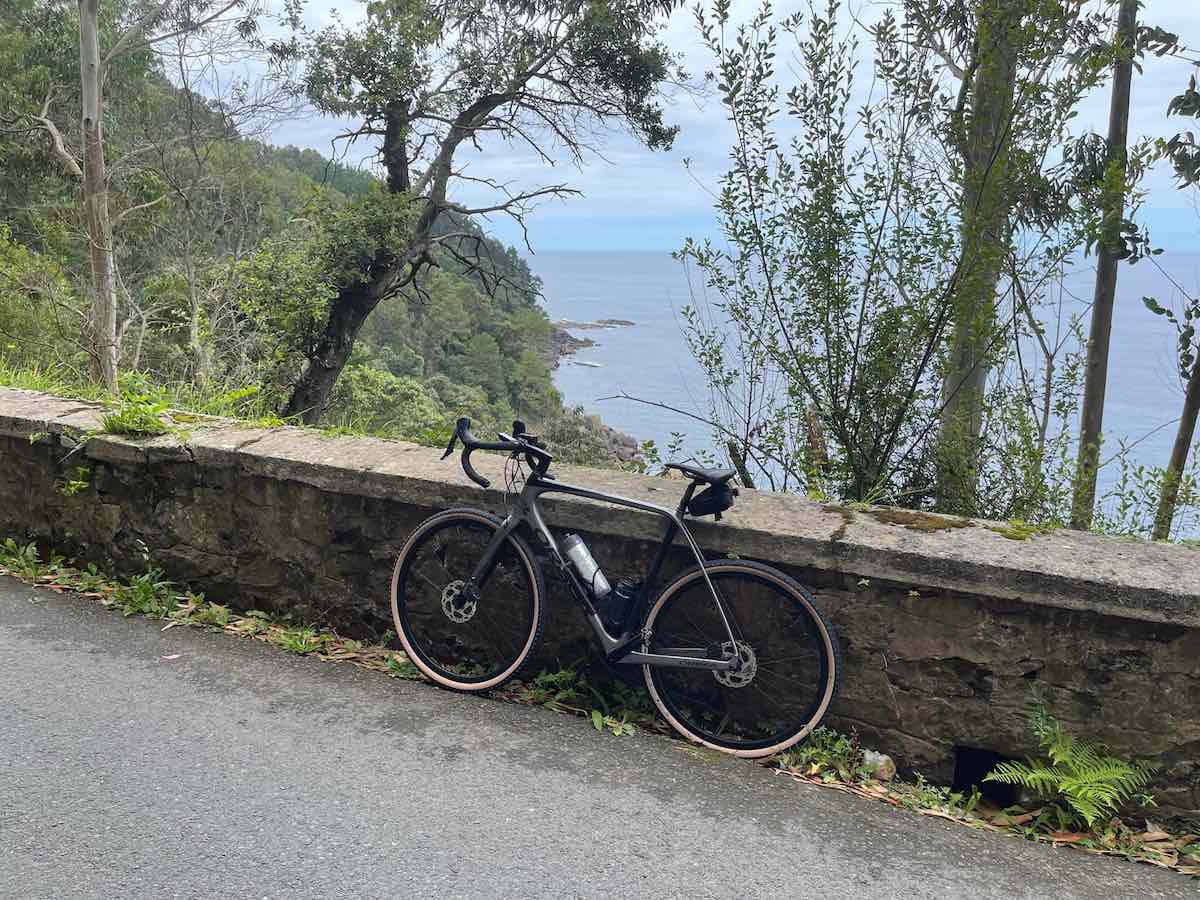 a bicycle leans against a low stone wall beside a road, beyond is the steep side of a mountain and the ocean.