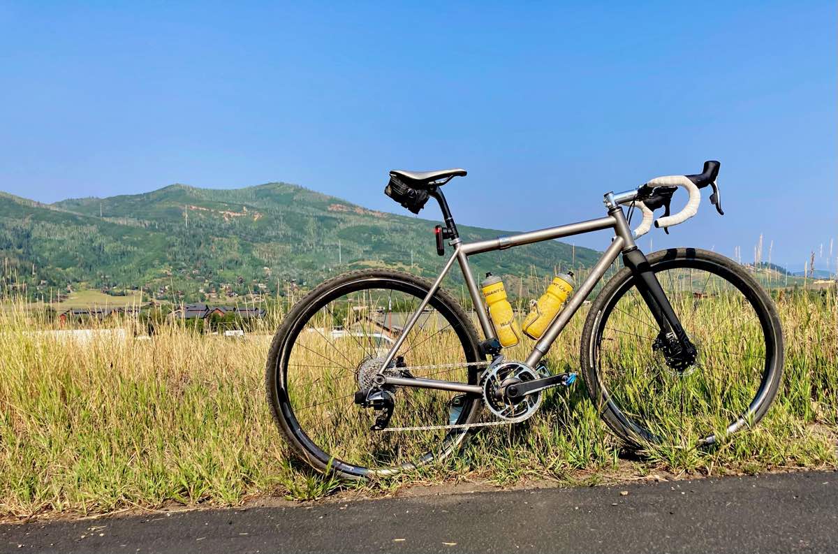 bikerumor pic of the day a bicycle is on the side of a road in golden brush with a gentle sloping green mountain in the background, the sky is clear and blue.