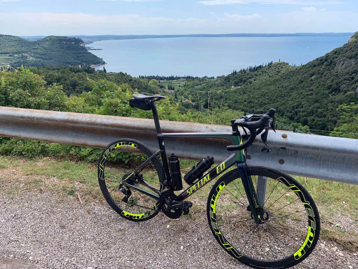 bikerumor pic of the day a road bike is leaning against a metal auto barrier on a road overlooking a large lake, there are a lot of green trees around the lake, the sky is blue with clouds on the horizon.