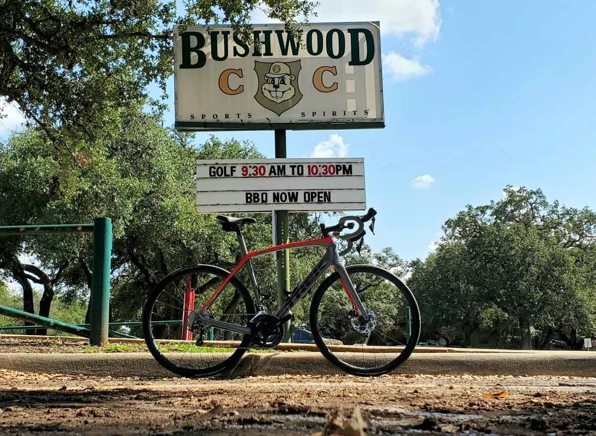 bikerumor pic of the day a bicycle is in front of a sign for brushwood country club bbq there is a picture of a gopher in the middle of the sign. the sky is blue with some clouds and there are trees in the background
