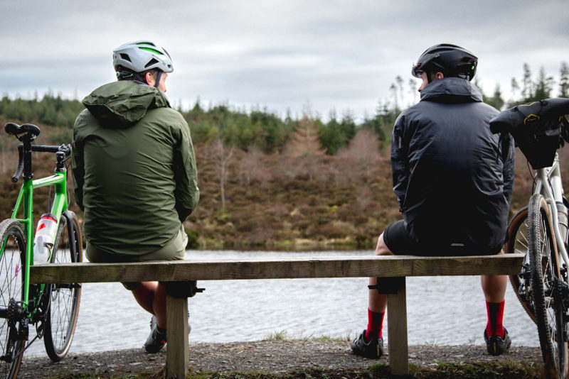 two men wearing endura gv500 coats sit facing the water next to bicycles