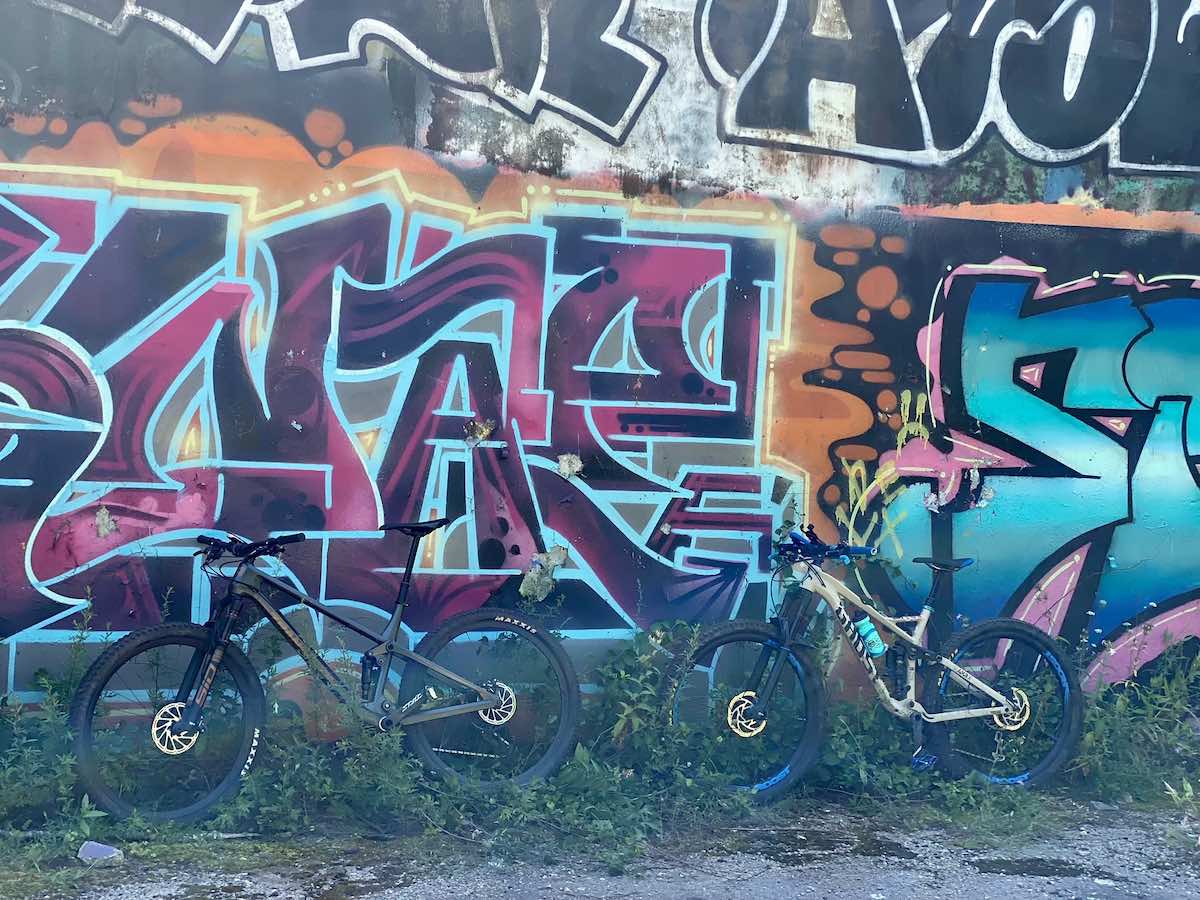 bikerumor pic of the day two mountain bikes lean against a concrete wall covered in colorful graffiti