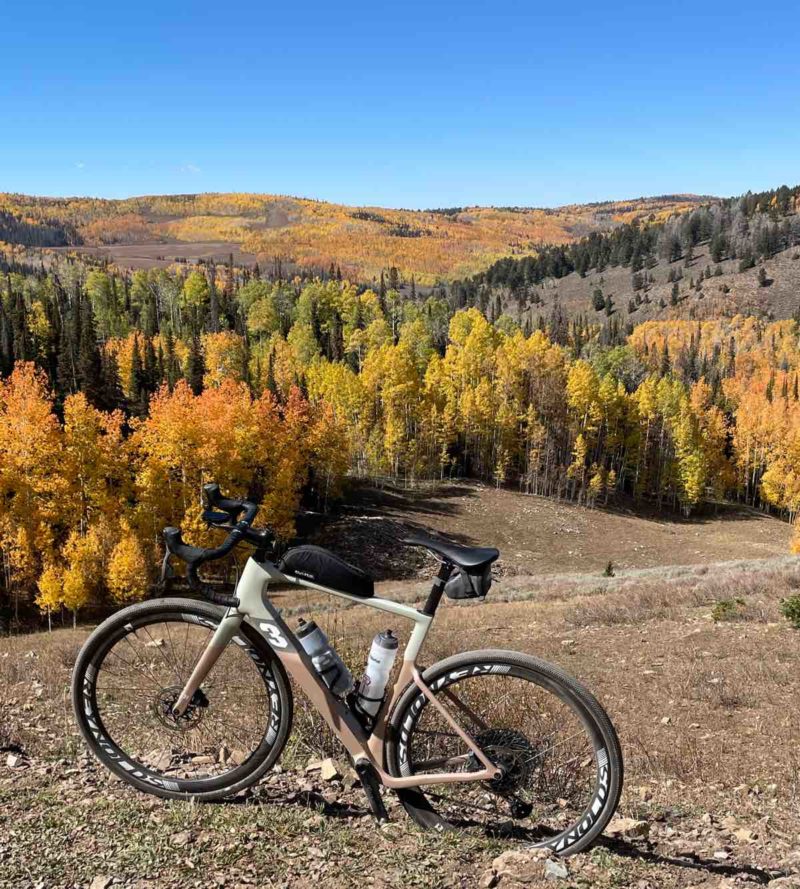 bikerumor pic of the day a bicycle is on a dirt clearing on the side of a low mountain, trees surround and have turned yellow for autumn, the sky is clear and blue.