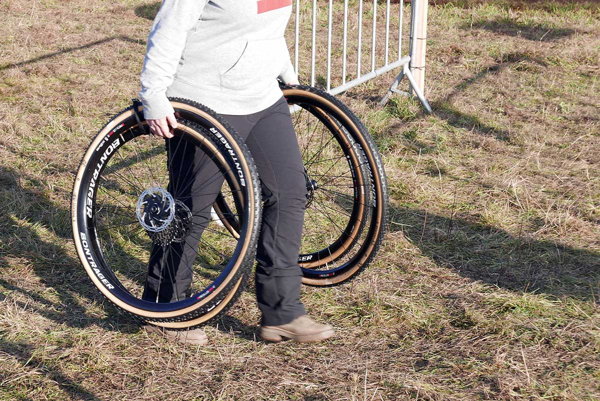 person carrying extra wheels and tires to the pits at a cyclocross race