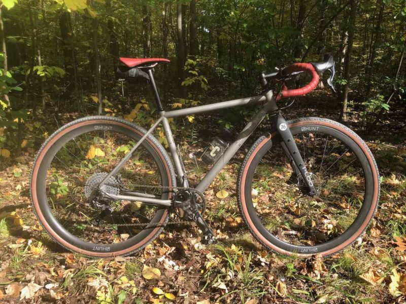 bikerumor pic of the day a grey colored bicycle with red seat and handlebars is posed near the woods where the leaves have turned their fall colors and some have fallen to the ground