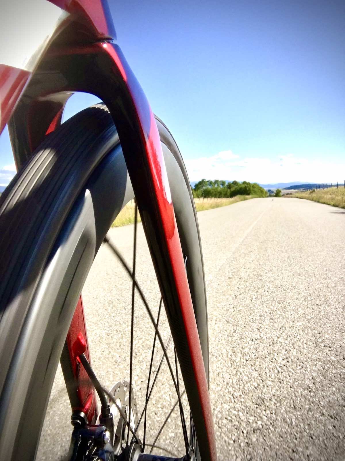 bikerumor pic of the day the photo is from the side of a road bike looking forward past the front wheel and fork towards the long straight road, the sky is clear and the sun is bright.