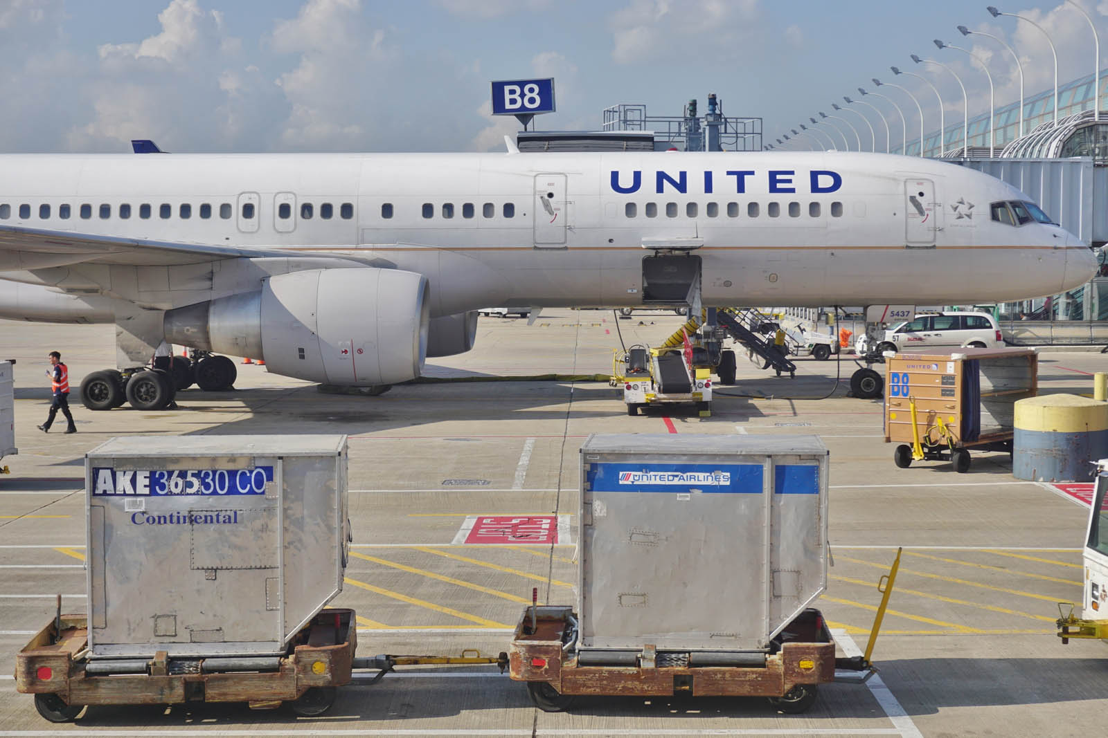 A United Airlines plane sits on the tarmac with baggage containers in the foreground