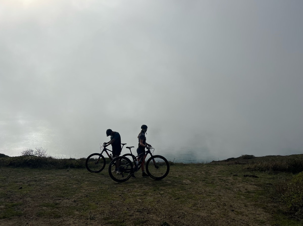 bikerumor pic of the day two cyclists on a clearing with clouds or fog behind them.