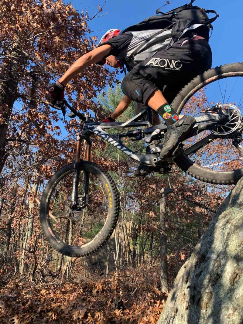 Bikerumor pic of the day Austin Liu rides a mountain bike down the side of a large granite rock, leaves on the trees behind have turned brown in autumn, the sky is bright blue and clear.