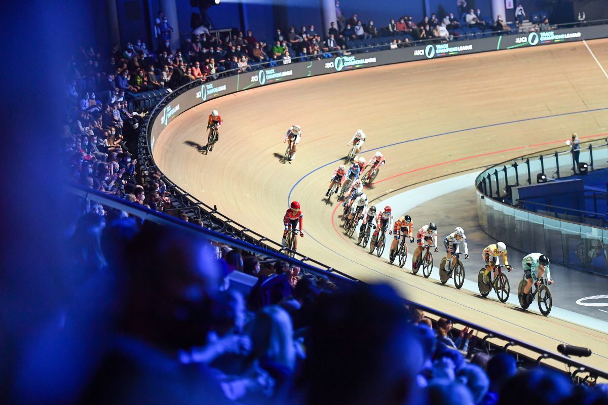 Track cyclists racing around a velodrome viewed from the stands.