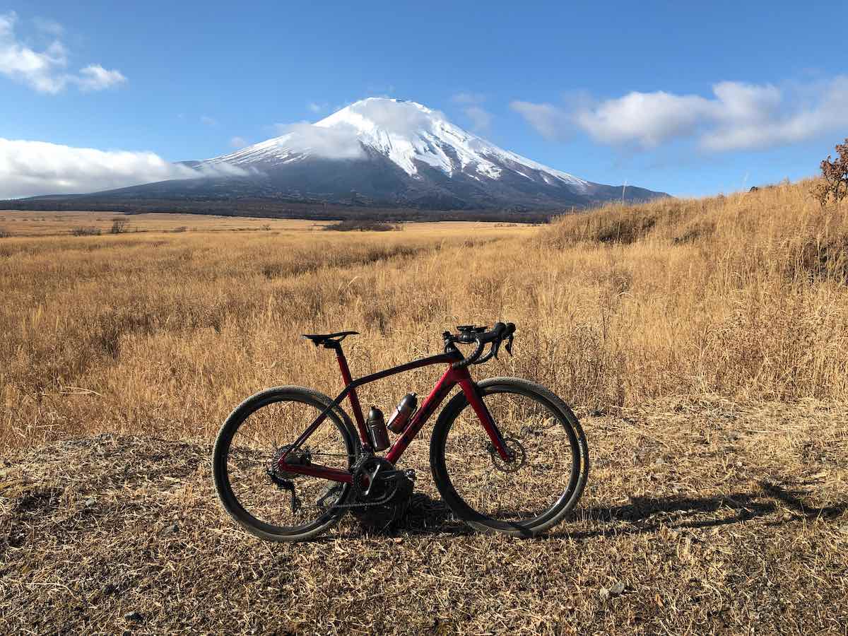 bikerumor pic of the day a read and black gravel bicycle is in the middle of a golden grassy field the sun is high and bright and mount fuji japan is in the distance.