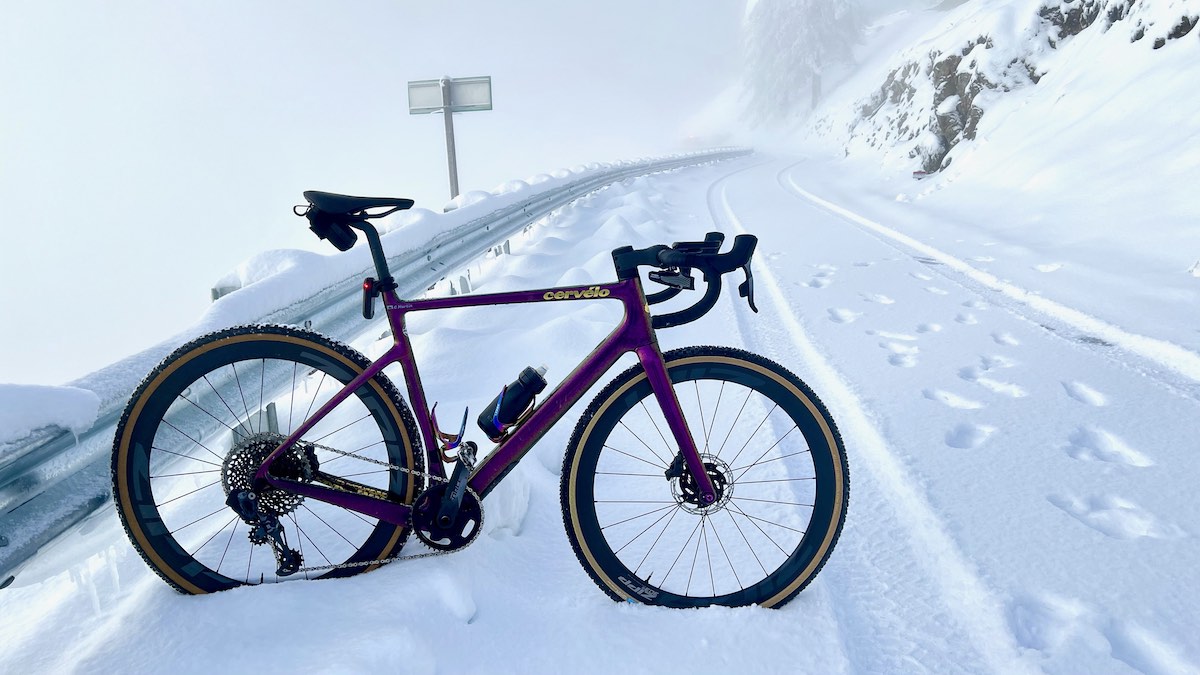 bikerumor pic of the day a bicycle is posed on a snow covered road leading up a hill, the snow is covering the mountain surrounding the road and the purple bicycle stands out nicely.