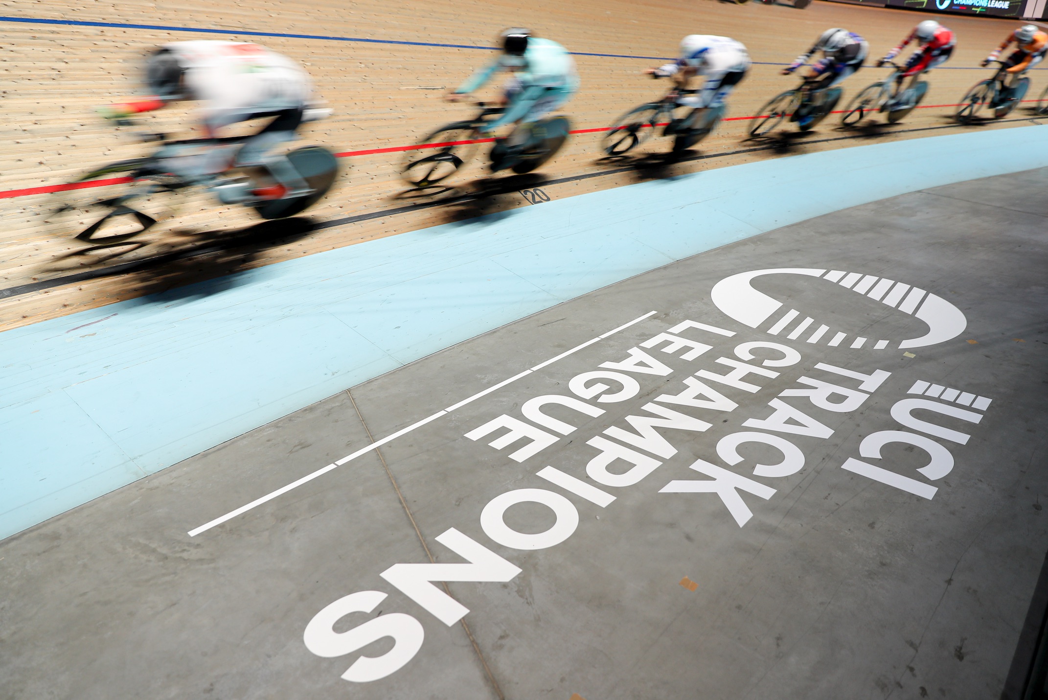 Track cyclists racing in a velodrome over the UCI Track Champions League logo.