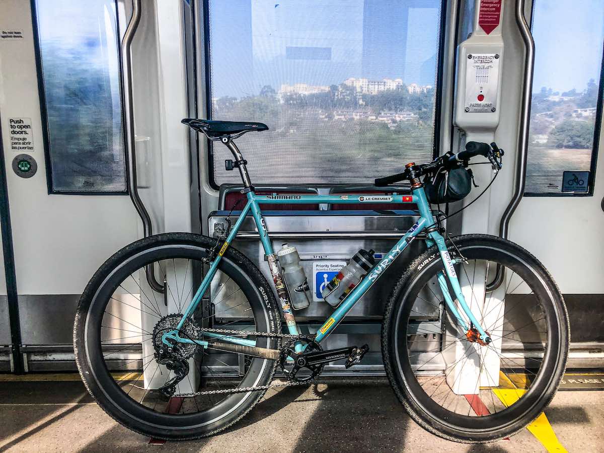 bikerumor pic of the day a teal colored bicycle leans against the inside of a subway car, sun is shining in from one side and you can see the city of san diego outside the window.