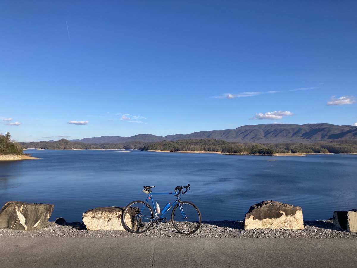bikerumor pic of the day a bicycle leans against a chunk of stone that borders a lake in the mountains, the sky is blue and there are a very few clouds over in the distance.