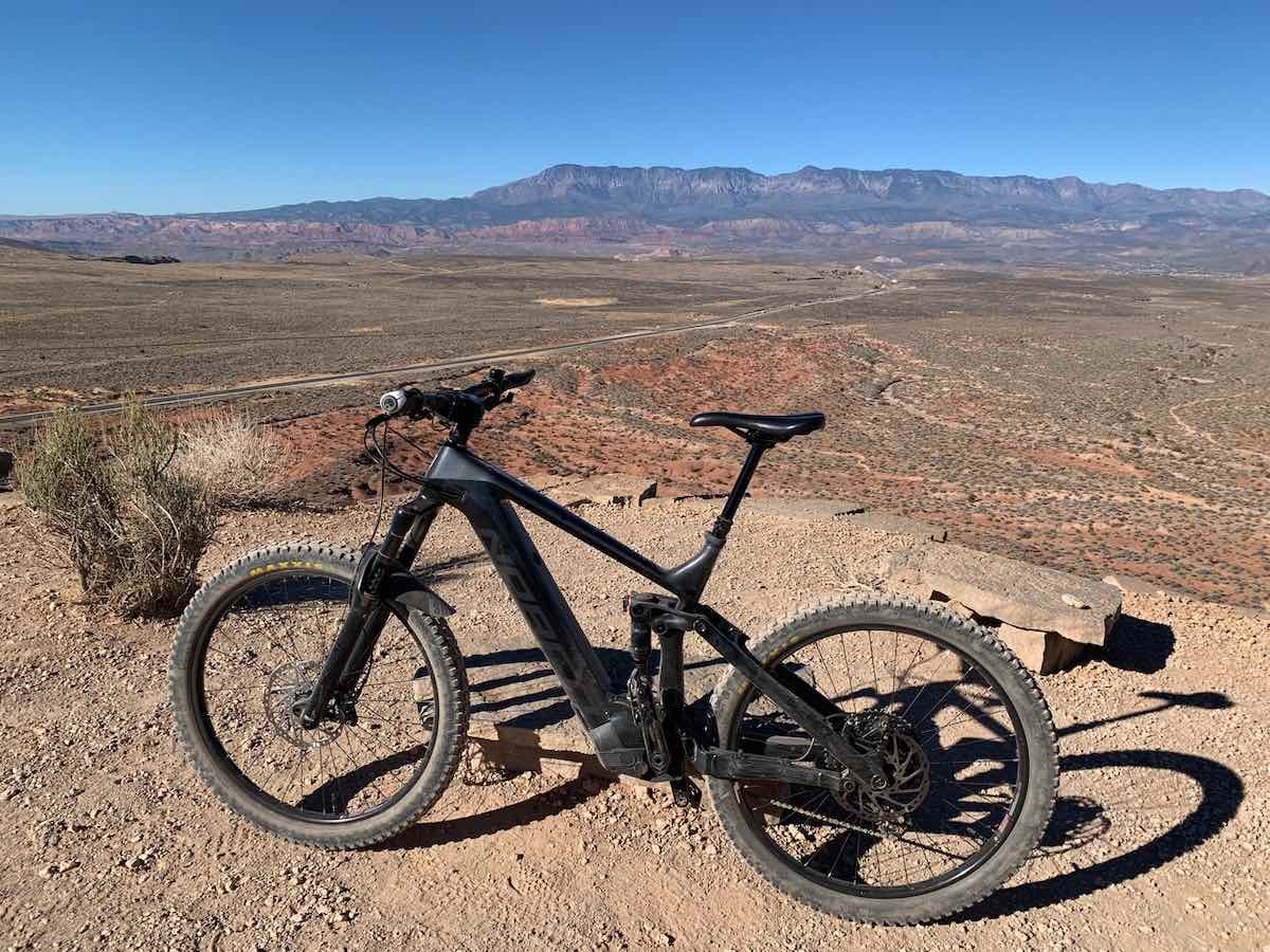 bikerumor pic of the day a electric assist mountain bike is at the top of a mesa looking out over a vast expanse of desert in st george utah, the sun is bright and there are no clouds in the sky.