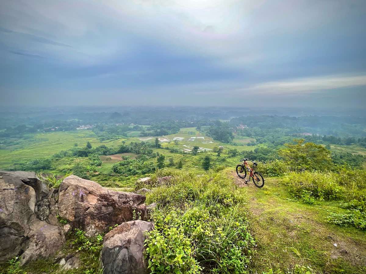 bikerumor pic of the day a bicycle is atop a green covered hill overlooking a green valley, the sky is cloudy and there is a peek of sun from above.