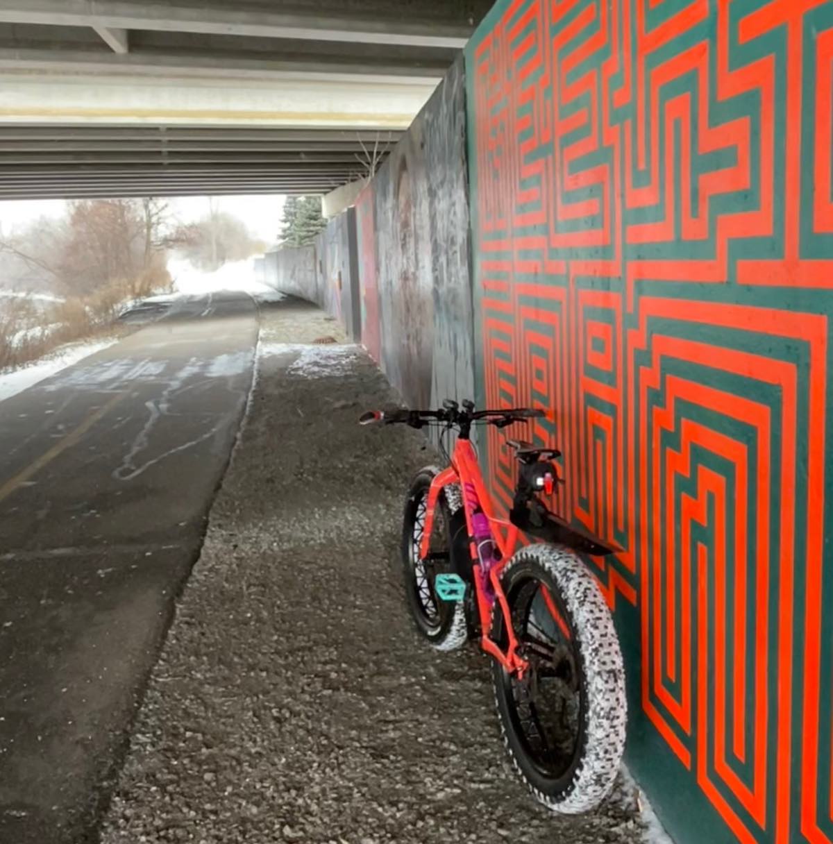 bikerumor pic of the day a fat bike with snow on its tires leans against a brightly painted geometric mural under an overpass in Lansing Michigan.