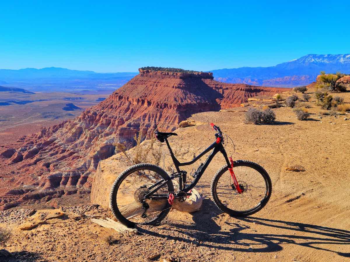 bikerumor pic of the day a mountain bike leans against a small rock atop a mesa in utah, the dirt is golden and red all around and the sky is bright and clear.