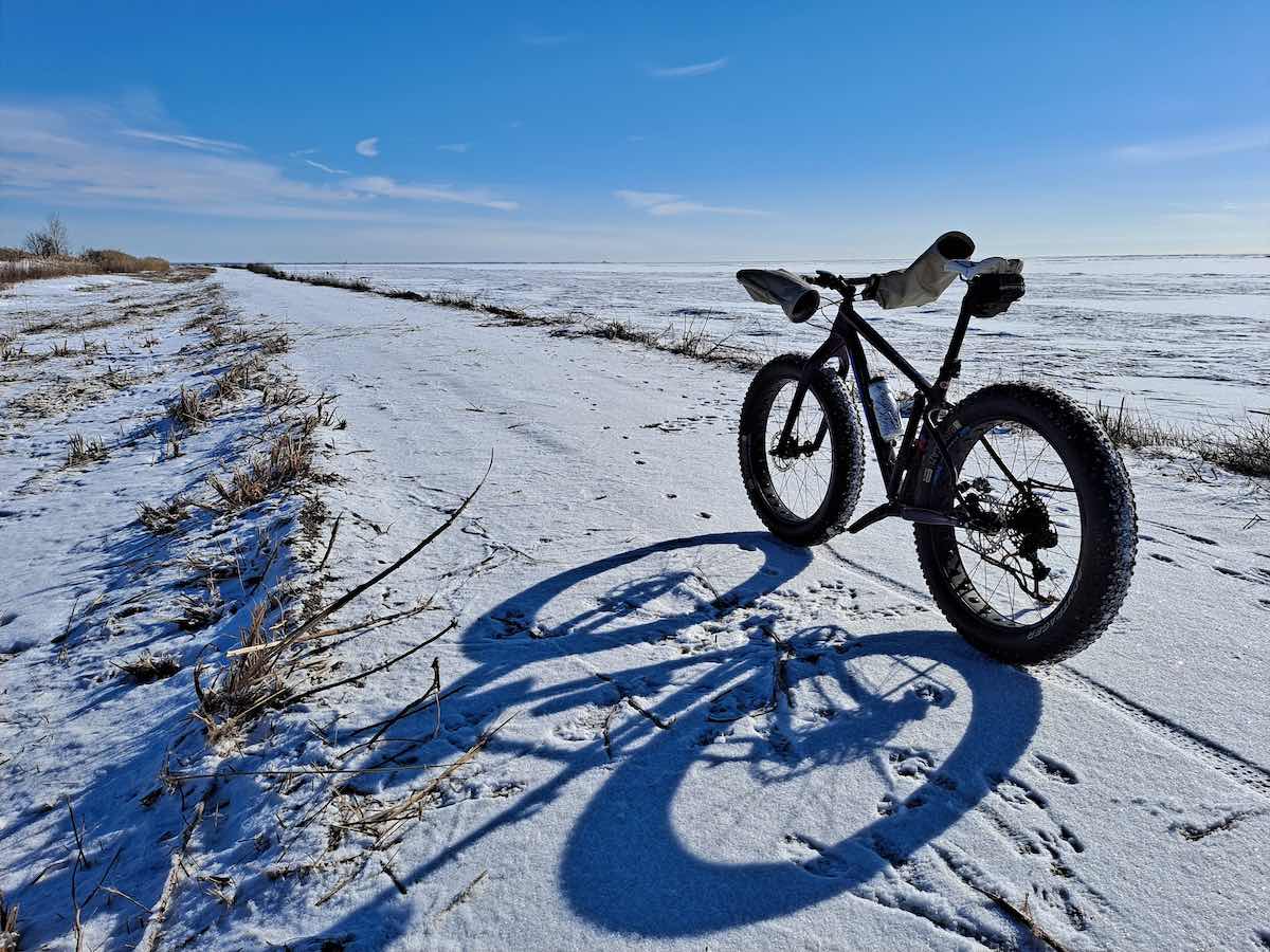 bikerumor pic of the day a fat tire bicycle is on a jetty along lake erie, the lake is frozen and there is a light covering of snow on the trail, the sun is low and creating a long shadow of the bike along the jetty.