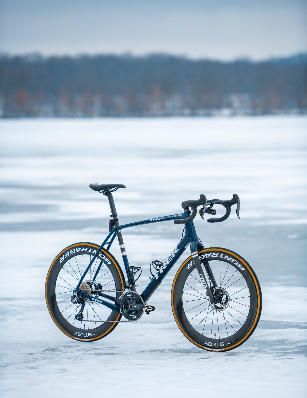 bikerumor pic of the day a gravel bike is posed on a frozen lake, the sky is covered in clouds and the day has a grey wash, there are trees in the distance at the end of the frozen lake.