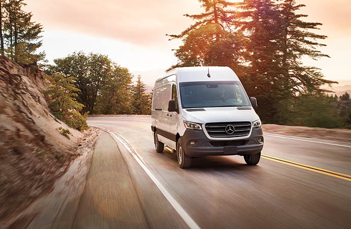 Mercedes-Benz Sprinter van driving on a road surrounded by trees.