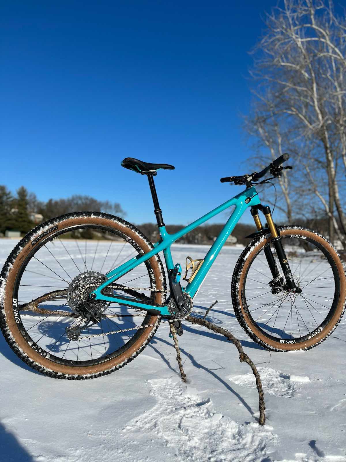 bikerumor pic of the day a mountain bike is posed on the snow in a clearing surrounded by trees, the sky is clear and bright