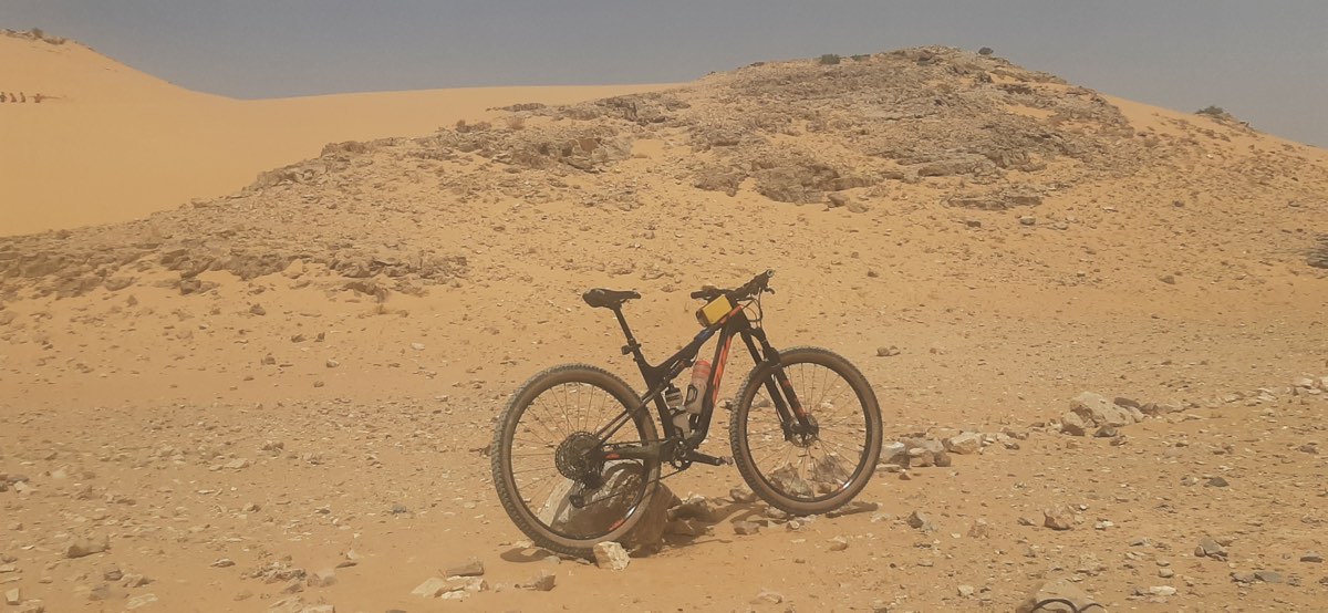 bikerumor pic of the day a mountain bike is on a sand dune, it is hazy and bright as if there is sand in the air.