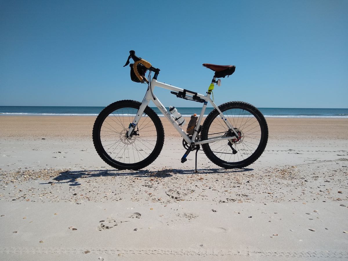 bikerumor pic of the day a mountain bike is on a flat sandy beach with a clear blue sky, the sun is high and the shadow of the bike is short