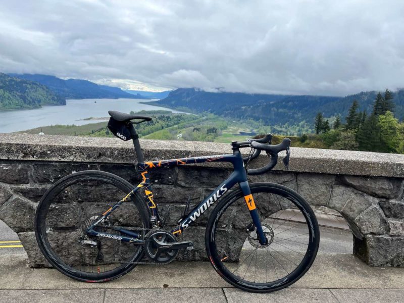 bikerumor pic of the day an s-works bicycle leans against a low stone wall overlooking a huge gorge with a river and green fields in the distance, the sky is bright and full of clouds.