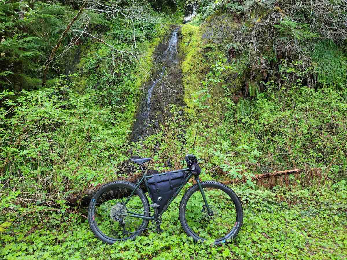 bikerumor pic of the day a mountain bike is in a lush green area at the base of a small waterfall.