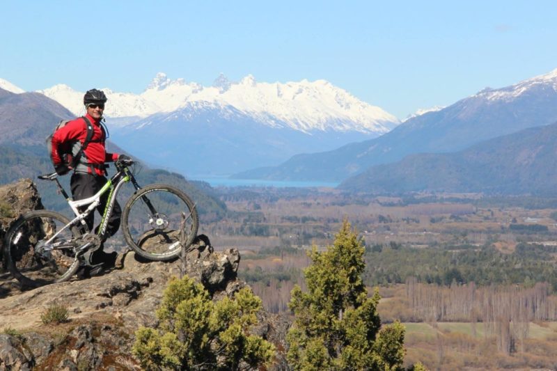 bikerumor pic of the day a mountain biker stands on the edge of a lookout over the region of el bolson in patagonia argentina, surrounded by snow capped mountains and a clear blue sky