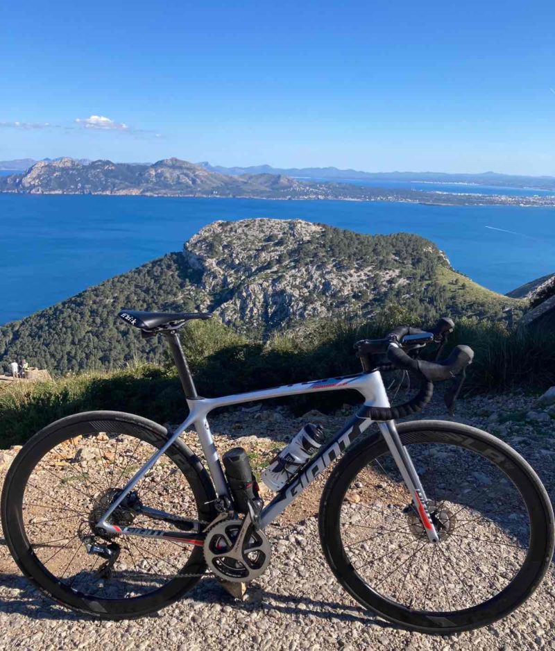 bikerumor pic of the day a bicycle is on the top of a rocky perch overlooking the sea, the sky i clear except for small wispy cloud in the distance.