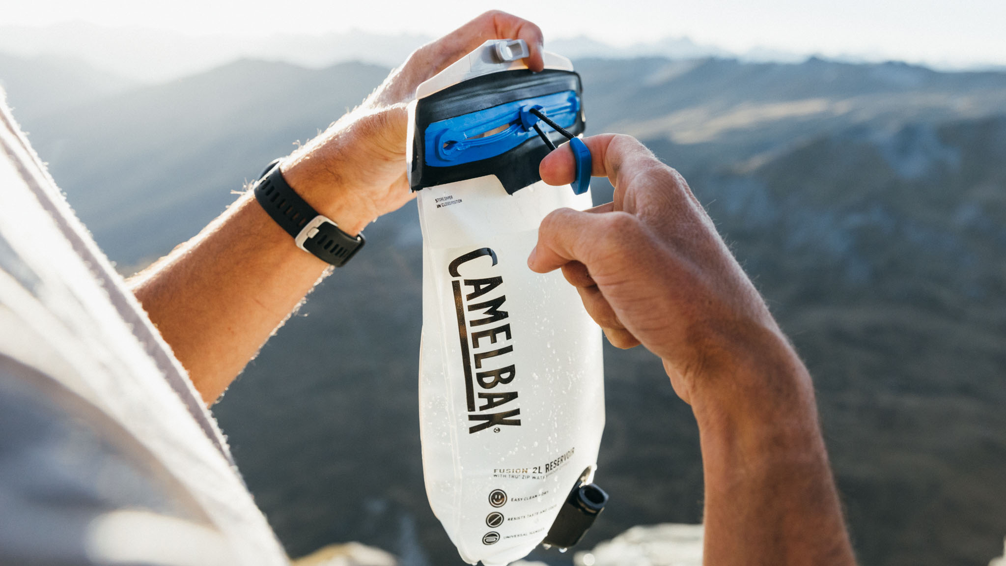 hands hold up the camelbak fusion in front of the camera with mountains in the background.