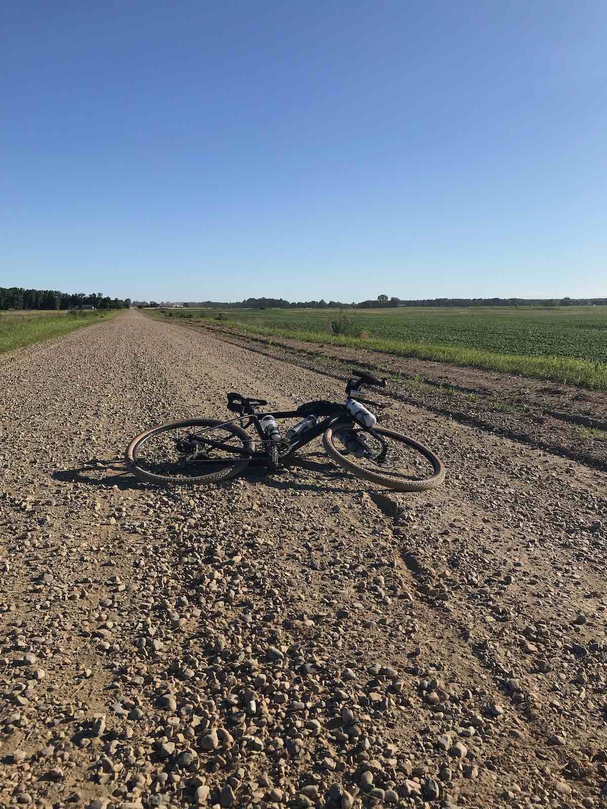 bikerumor pic of the day a bicycle lays on its side on a long straight gravel road the sky is clear and the sun is low