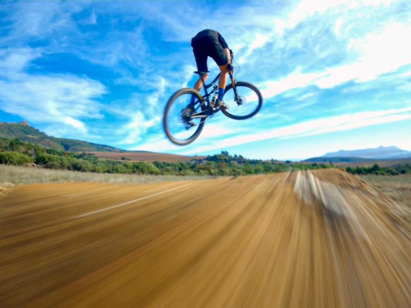 bikerumor pic of the day a cyclist is suspended mid jump over a dirt track with bright blue sky and clouds above.