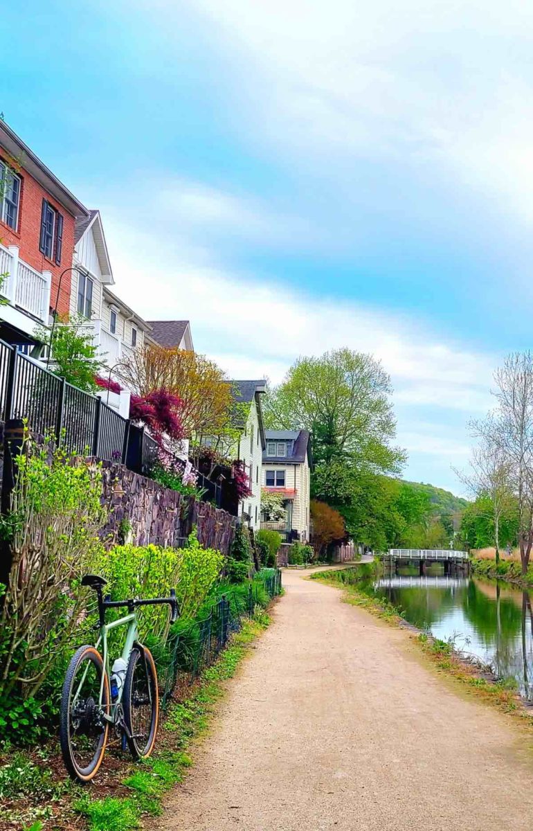 bikerumor pic of the day a bicycle is on a gravel tow path along a canal, there is a row of houses alongside the path and a small bridge spanning the canal in the distance.