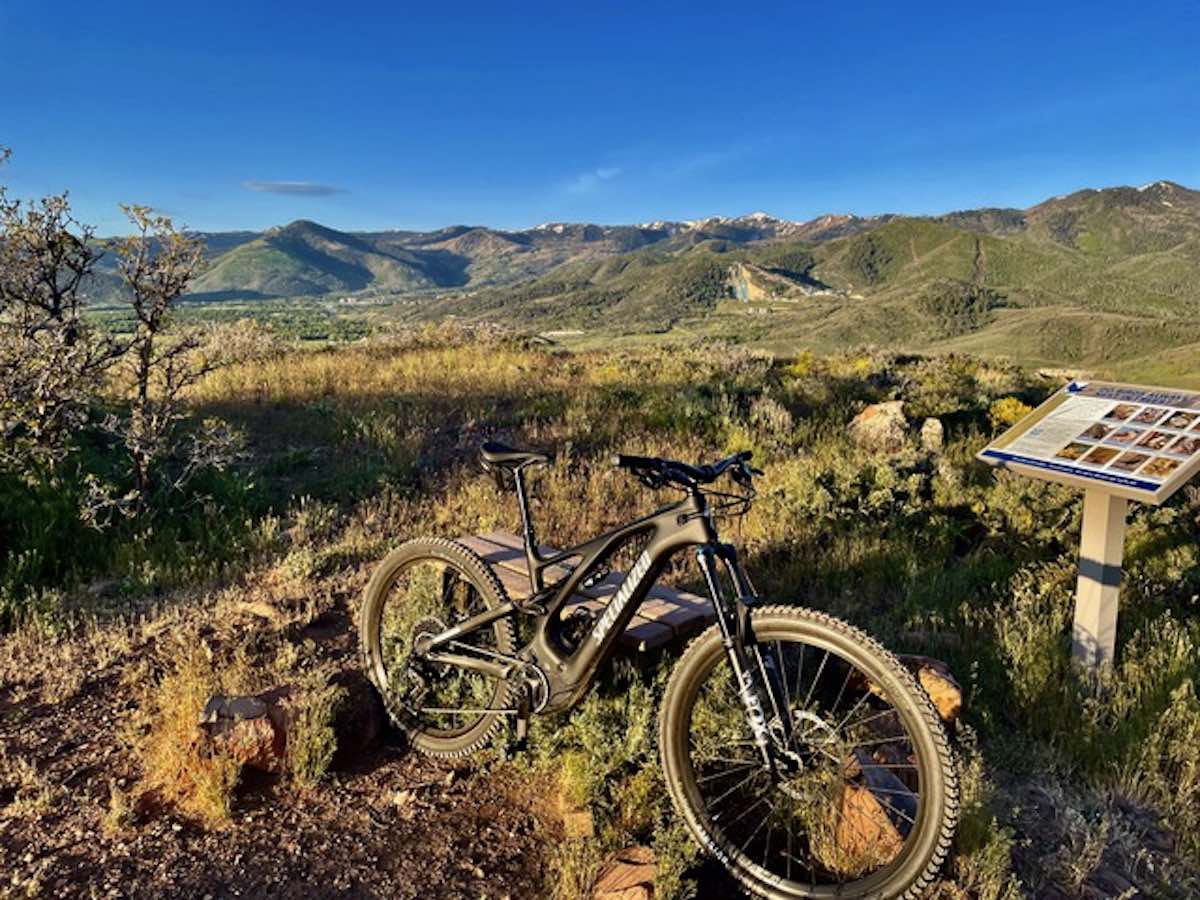 bikerumor pic of the day a mountain bike is posed among short brush in a valley surrounded by by low peaked mountains, the sun is low and the sky is clear