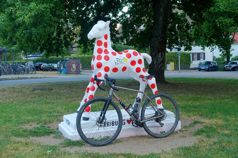 bikerumor pic of the day a bicycle leans against a sculpture of a baby horse that has been painted white with red dots it is in the middle of a town square