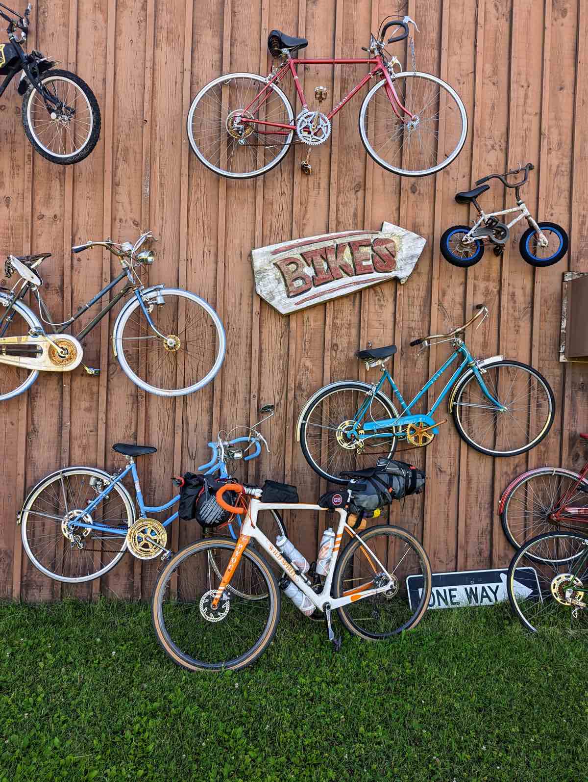 bikerumor pic of the day a bicycle is posed in front of a wood wall that has bicycles hung all over it and a sign in the shape of an arrow that says "bikes"