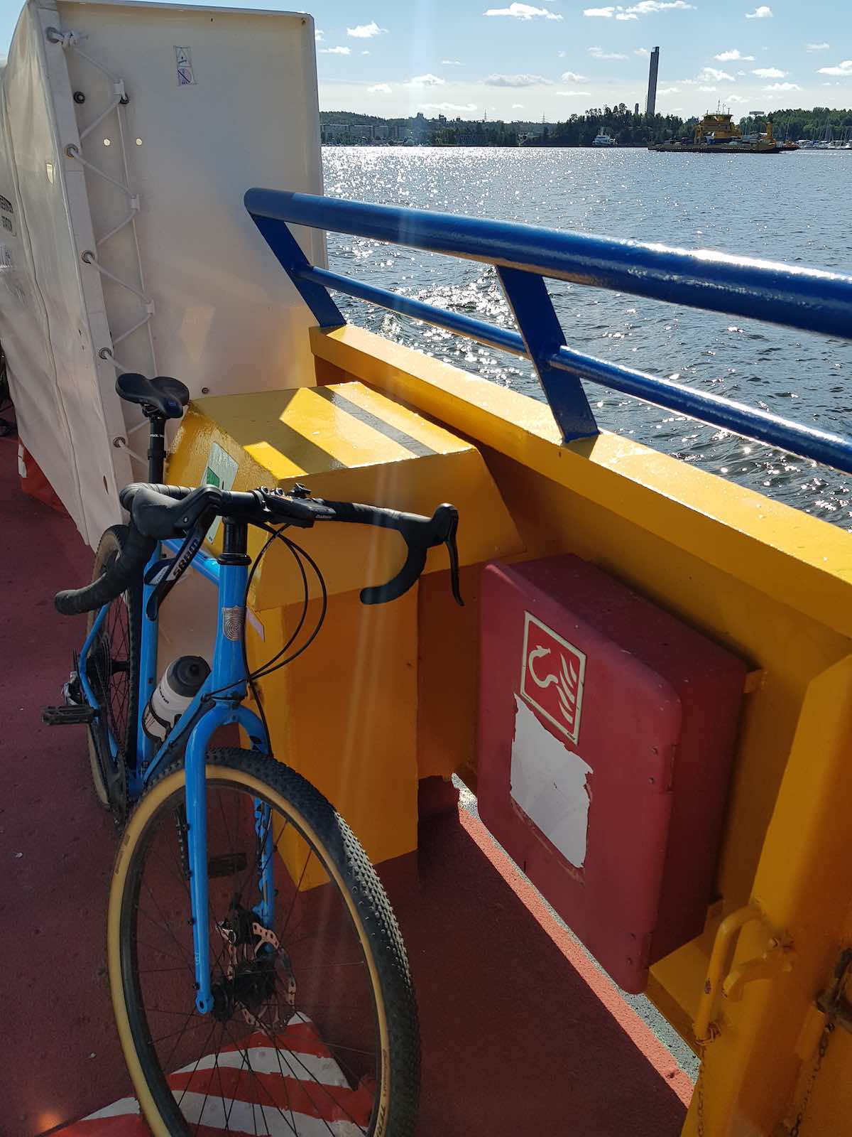 bikerumor pic of the day a blue road bike leans against the side of a ferry overlooking the water and a small city waterfront .
